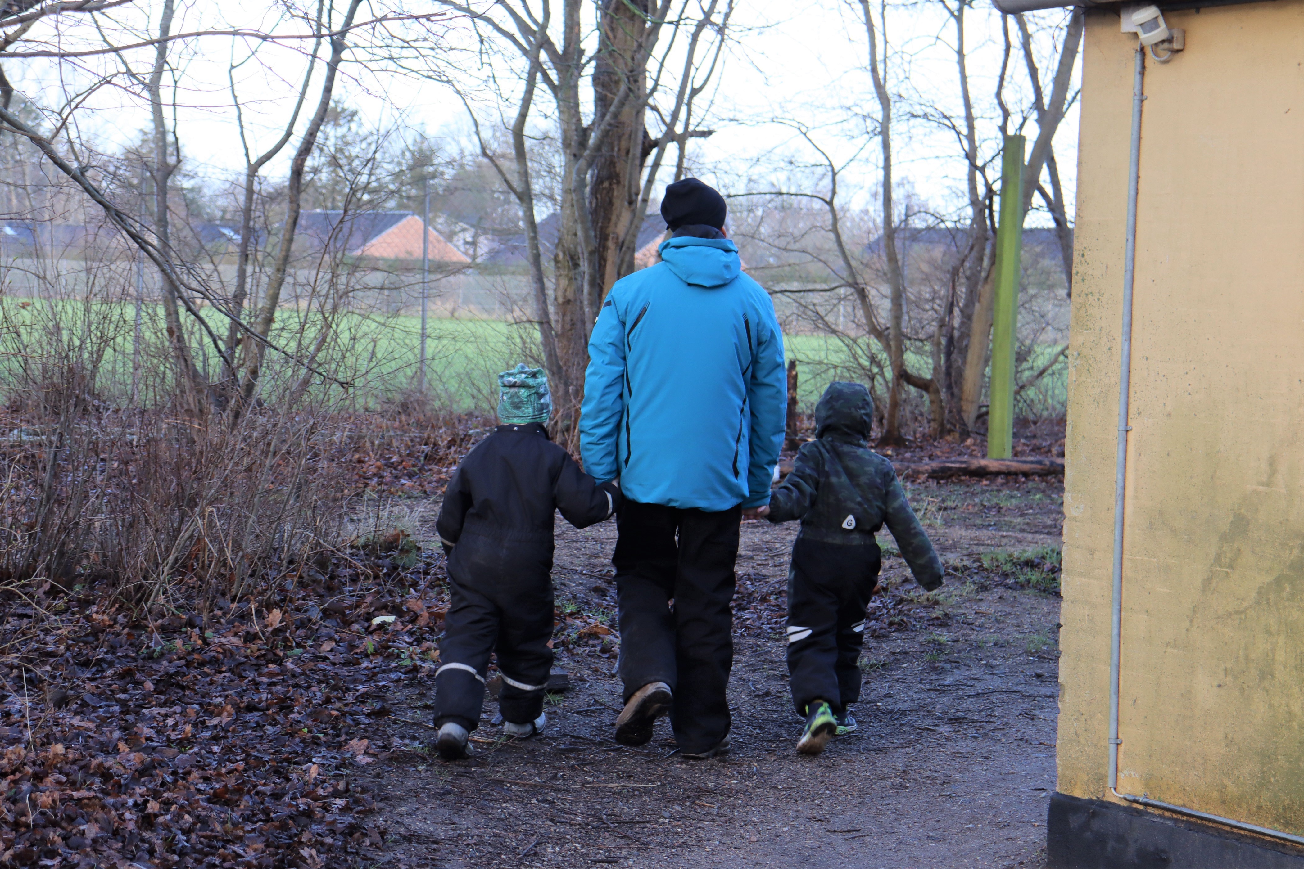 Pædagog går hånd i hånd med to børn, på vej ud i naturområde