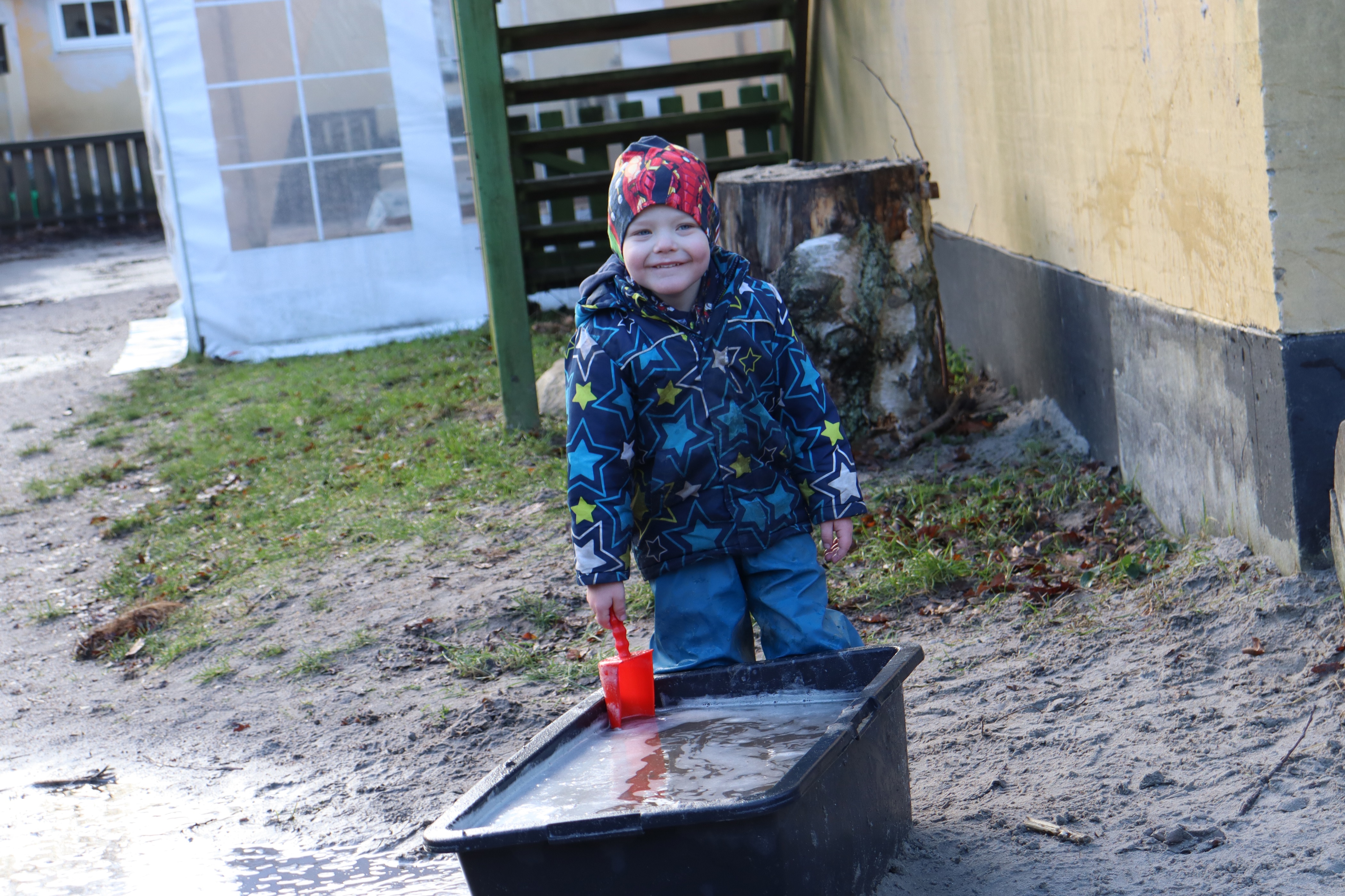 Dreng leger med vand i kasse, og smiler stort til kameraet