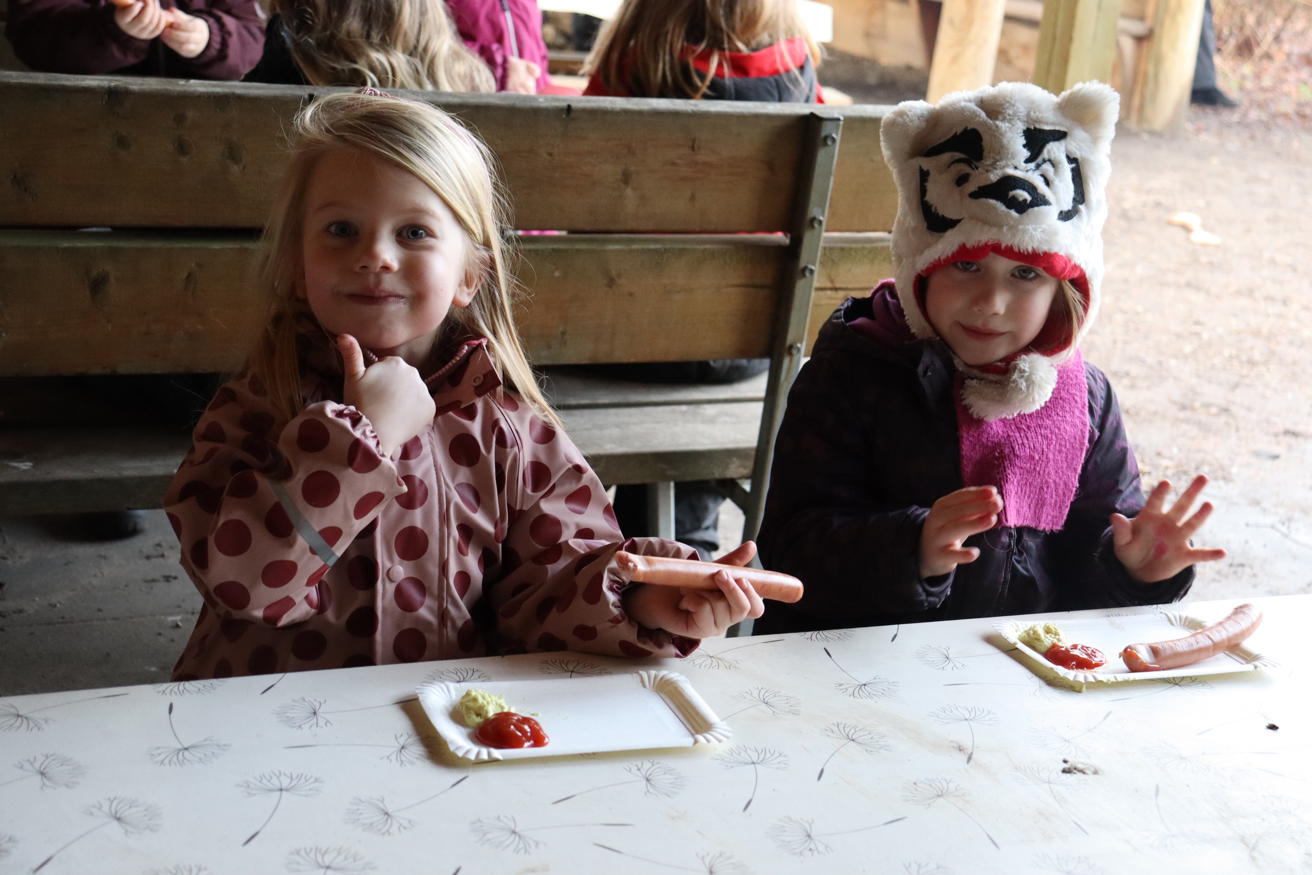 To piger spiser pølser med brød, udenfor - med thumbs-up fra den ene pige