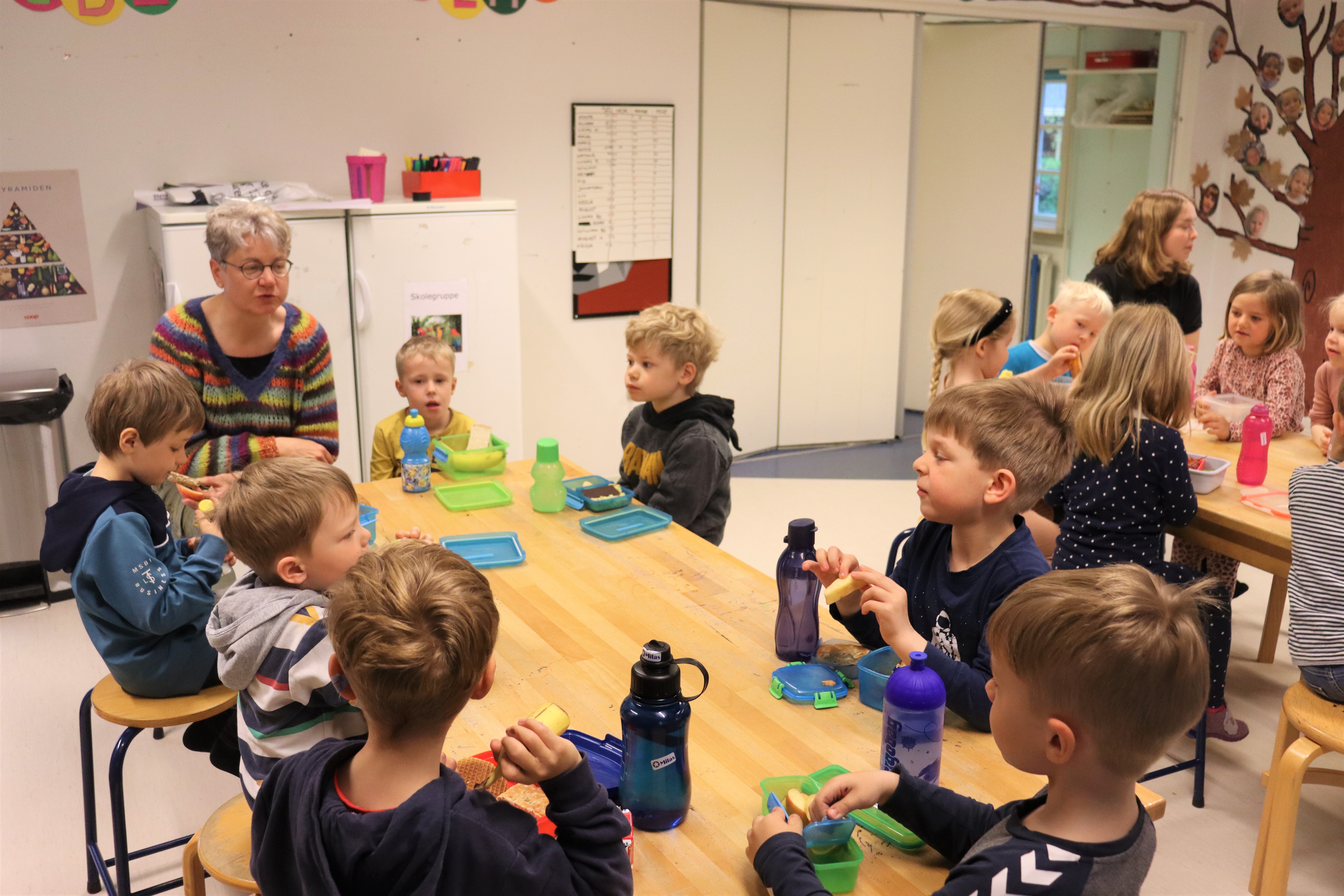 Børn sidder med pædagog rundt om bordet, og sidder og spiser